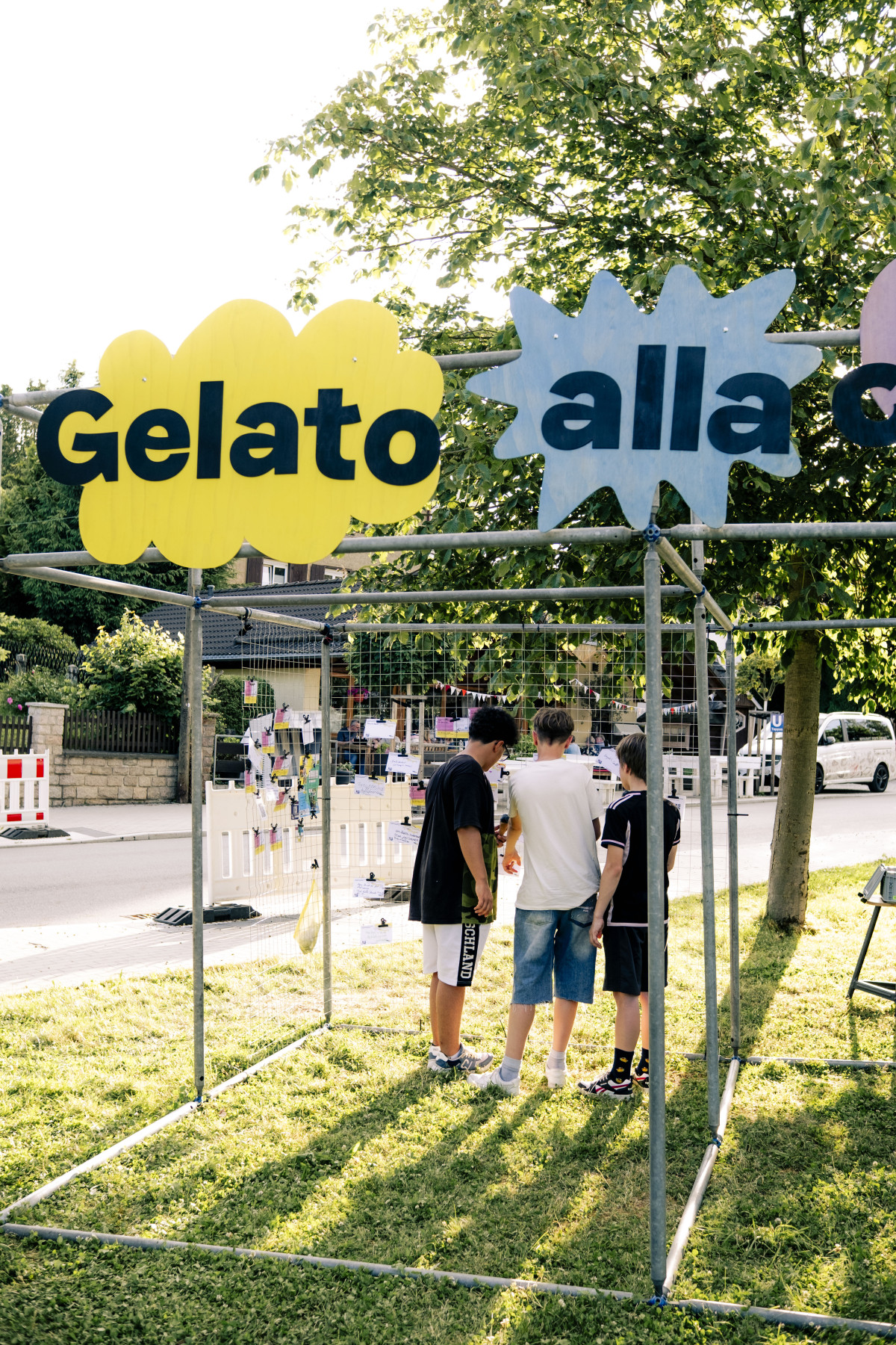Schilder mit der Aufschrift Gelato alla, drei Jugendliche stehen am Gerüst